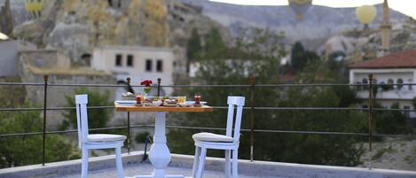 Una mesa con sillas en una terraza con vistas a un paisaje rocoso con edificios y globos aerostáticos al fondo.