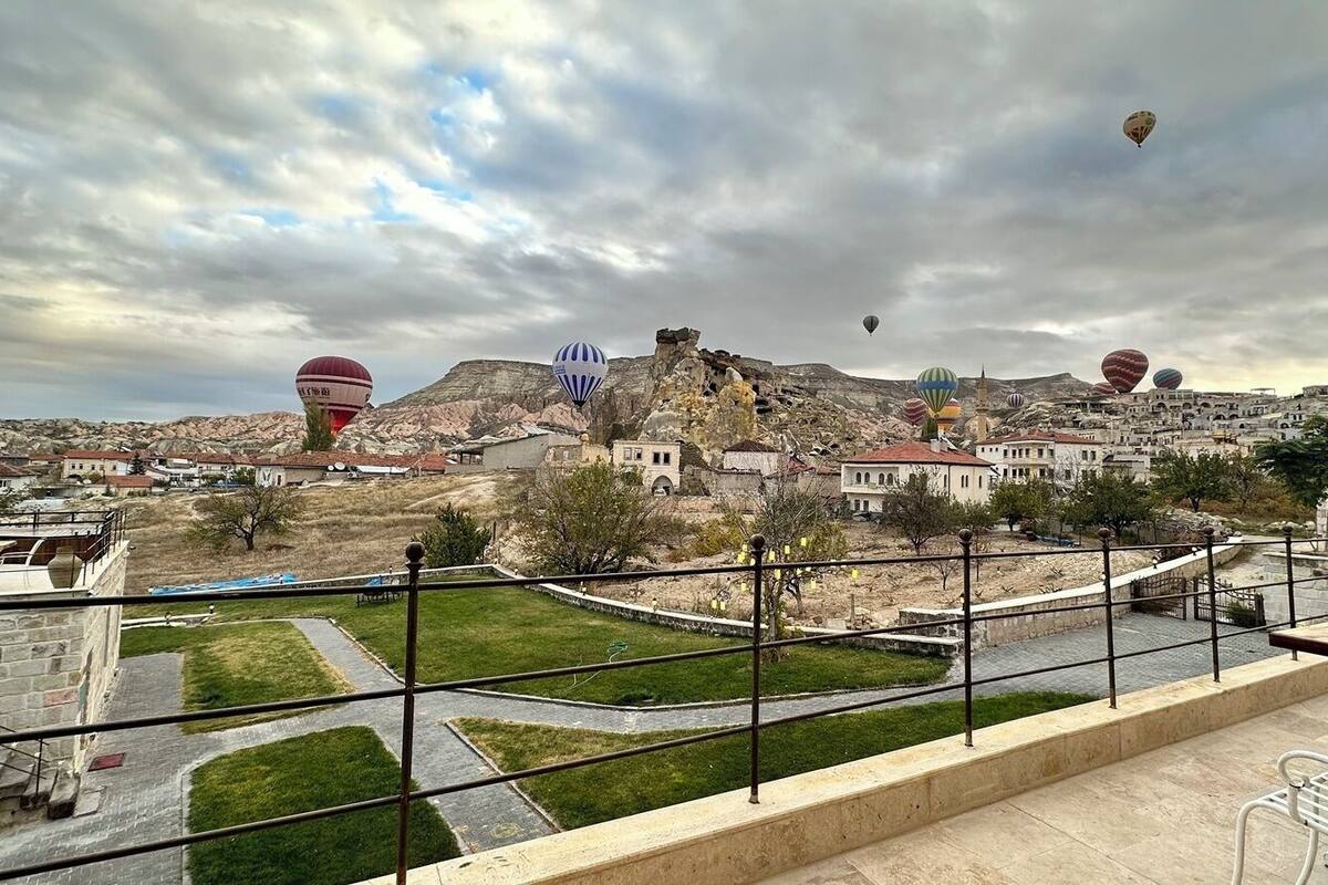 Vista de un pueblo con globos aerostáticos en el cielo, un área verde y edificios al fondo.