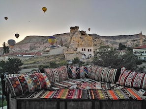 A traditional sofa with colorful, patterned cushions in a mountainous area with a historic building in the background. - Jacob's Cave Suites (Avanos)