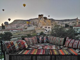 Un sofá tradicional con cojines de colores y estampados en una zona montañosa con un edificio histórico al fondo.