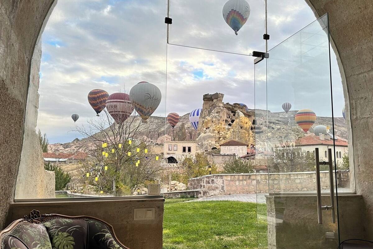 Una habitación con un amplio ventanal que da a un pueblo histórico con arquitectura tradicional y globos aerostáticos en el cielo.