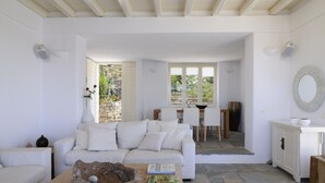 Un vaste espace de vie comprenant un canapé blanc, une table basse avec des livres, une table à manger avec des chaises et une cheminée en pierre.