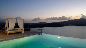 Un espace paisible au bord de la piscine, doté d’un lit à baldaquin offrant une vue sur une étendue d’eau calme et des montagnes lointaines.