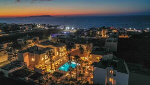 A resort with a pool, palm trees, and a view of the sea at dusk.