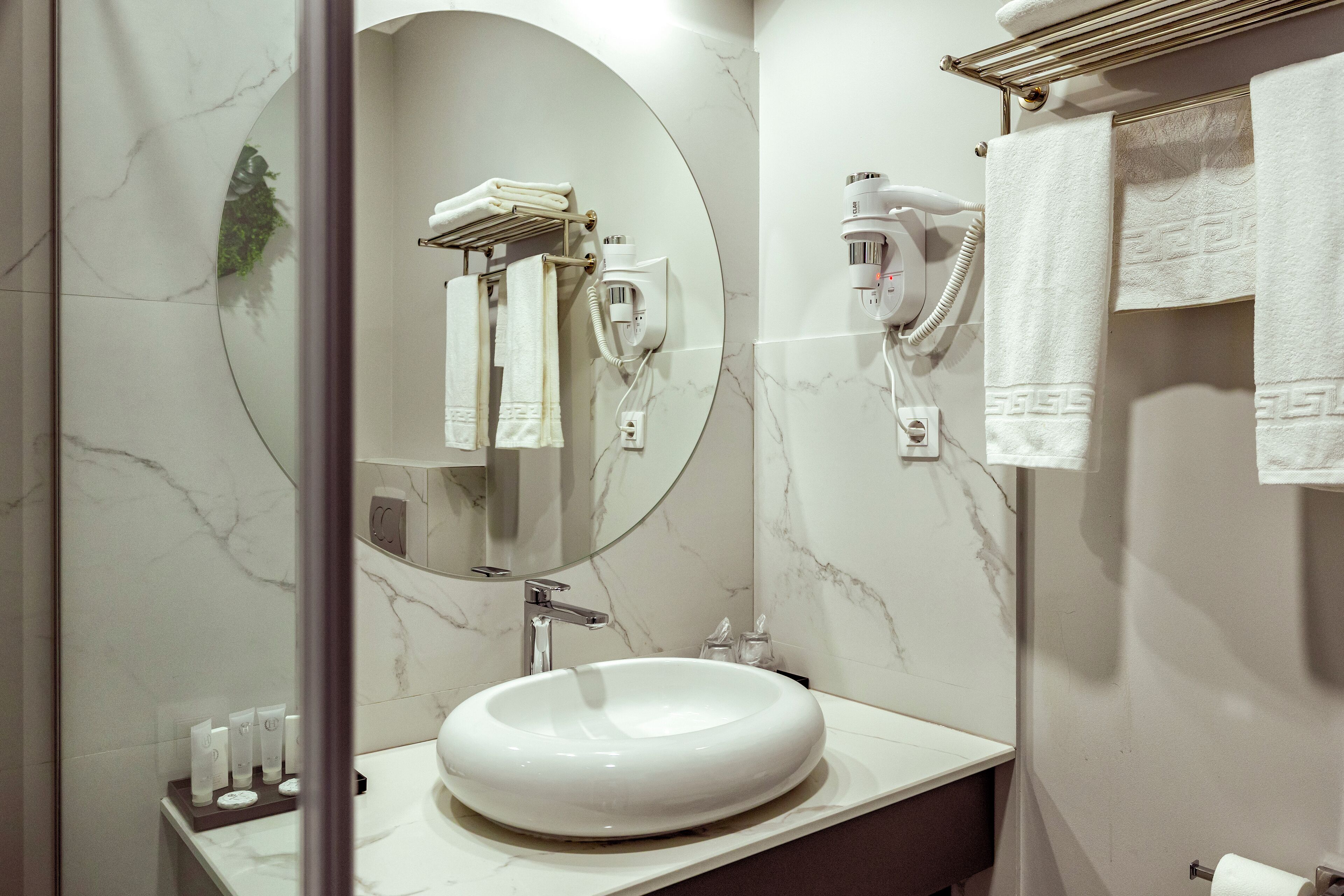 A modern bathroom with a large oval sink, a mirror, a towel rack, and a hairdryer mounted on the wall.