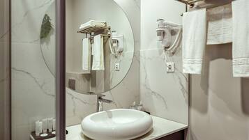 A modern bathroom with a large oval sink, a mirror, a towel rack, and a hairdryer mounted on the wall.