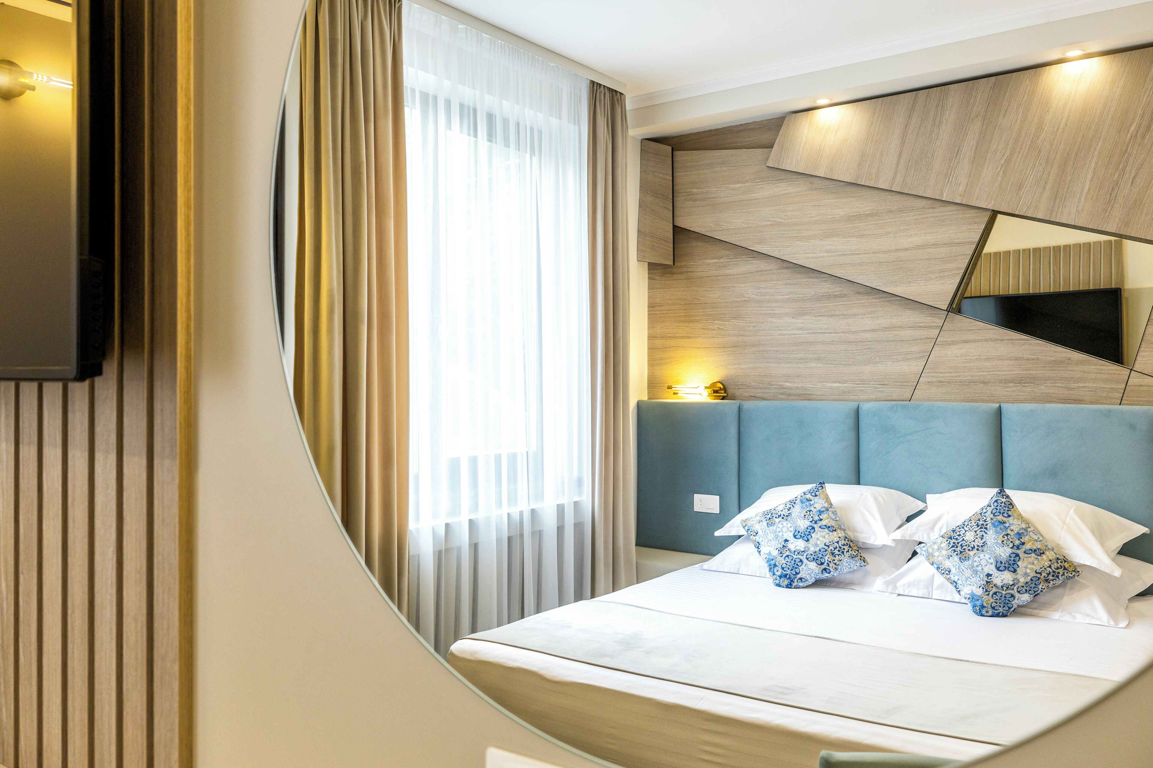 A modern hotel room with a bed, a TV mounted on the wall, and a large window with curtains.