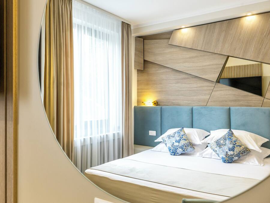 A modern hotel room with a bed, a TV mounted on the wall, and a large window with curtains.