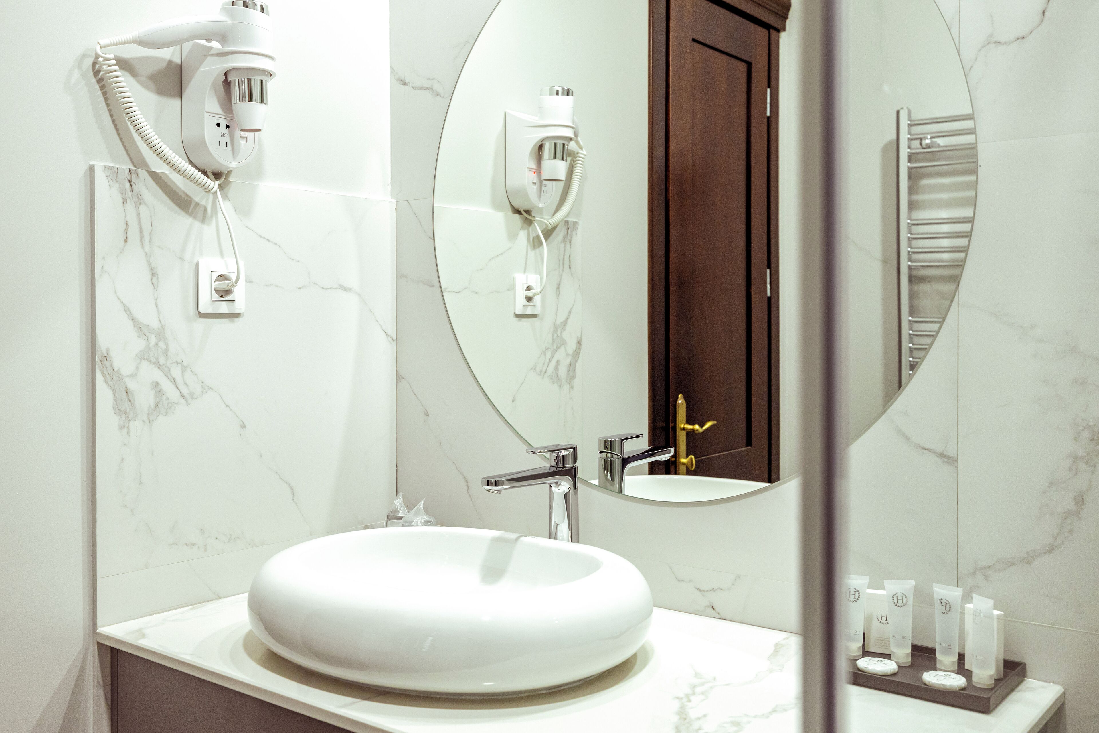 Un baño con un lavabo blanco y redondo, un espejo y un secador de pelo fijado en la pared.