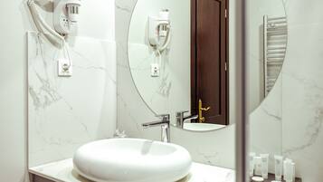 Un baño con un lavabo blanco y redondo, un espejo y un secador de pelo fijado en la pared.