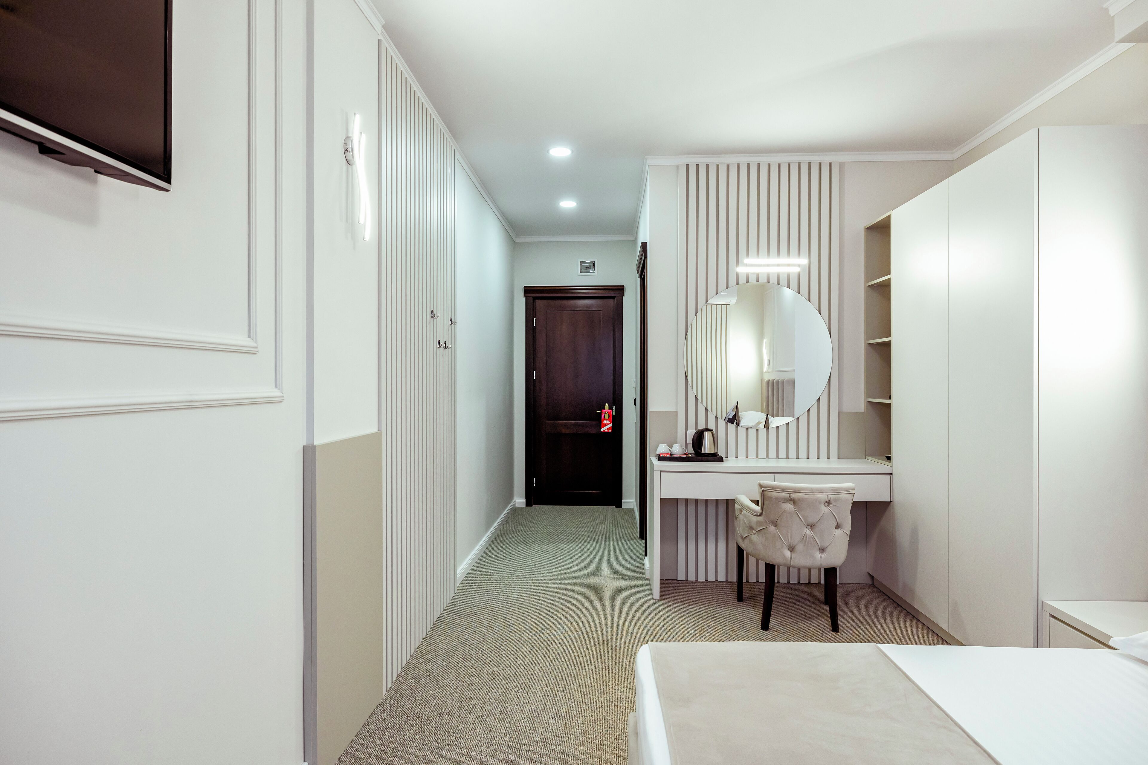 A hotel room with a bed, a desk with a chair, a wardrobe, and a mirror.