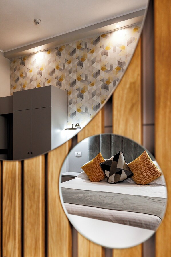 Un dormitorio moderno con una pared de estampado geométrico, un armario gris y una cama con almohadones estampados.