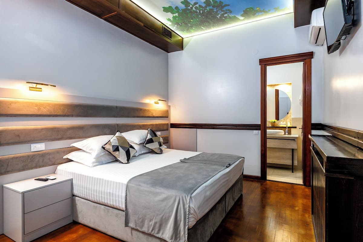 Un dormitorio moderno con cama, mesitas de noche, un espejo y un techo con diseño de hojas.