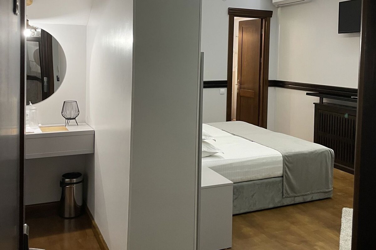 A modern bedroom with a bed, a mirror, a small table, and a ceiling mural.