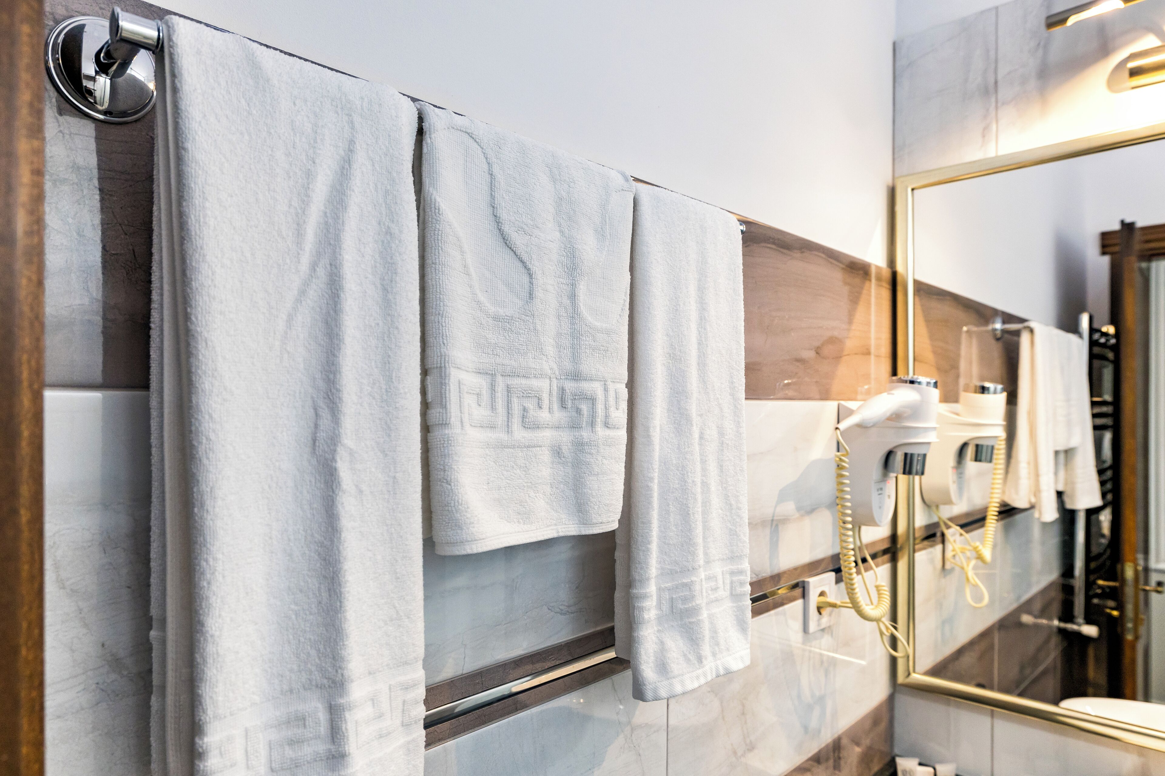 A bathroom with white towels hanging on a rack, a hairdryer, and a mirror with a wooden frame.