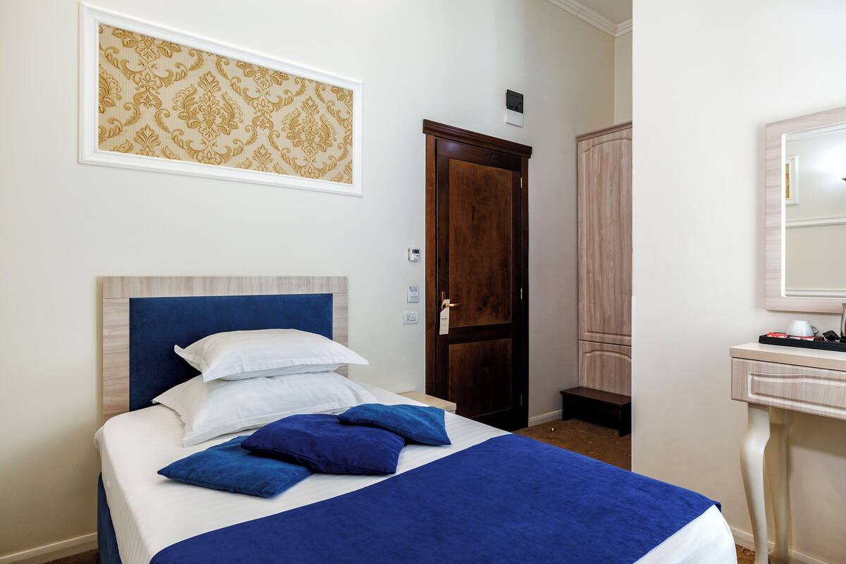 Una cama bien hecha con ropa de cama azul y blanca, un armario de madera y una mesita de noche con una lámpara.