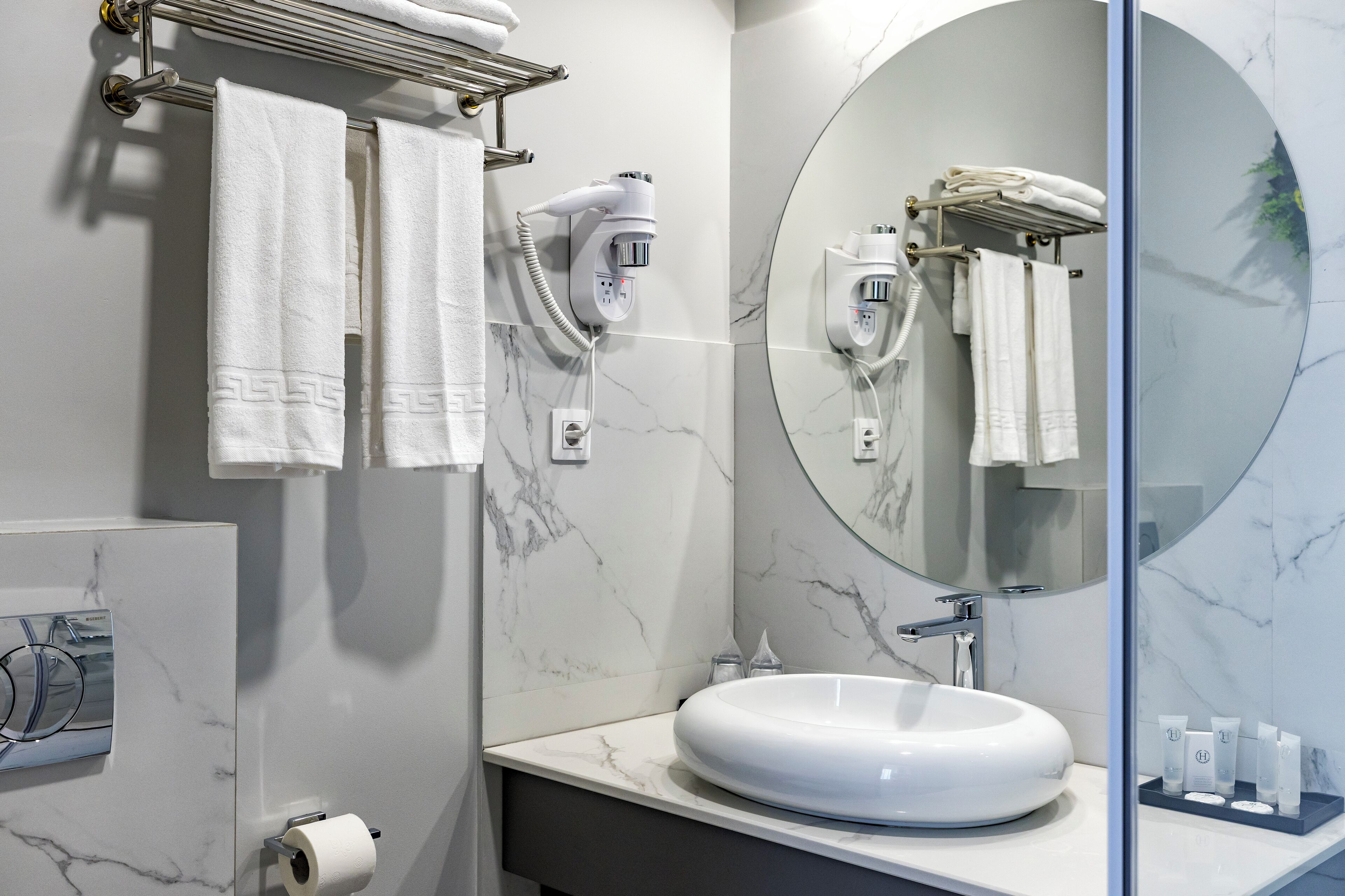 A modern bathroom with a marble sink, towel rack, hairdryer, and a large mirror.