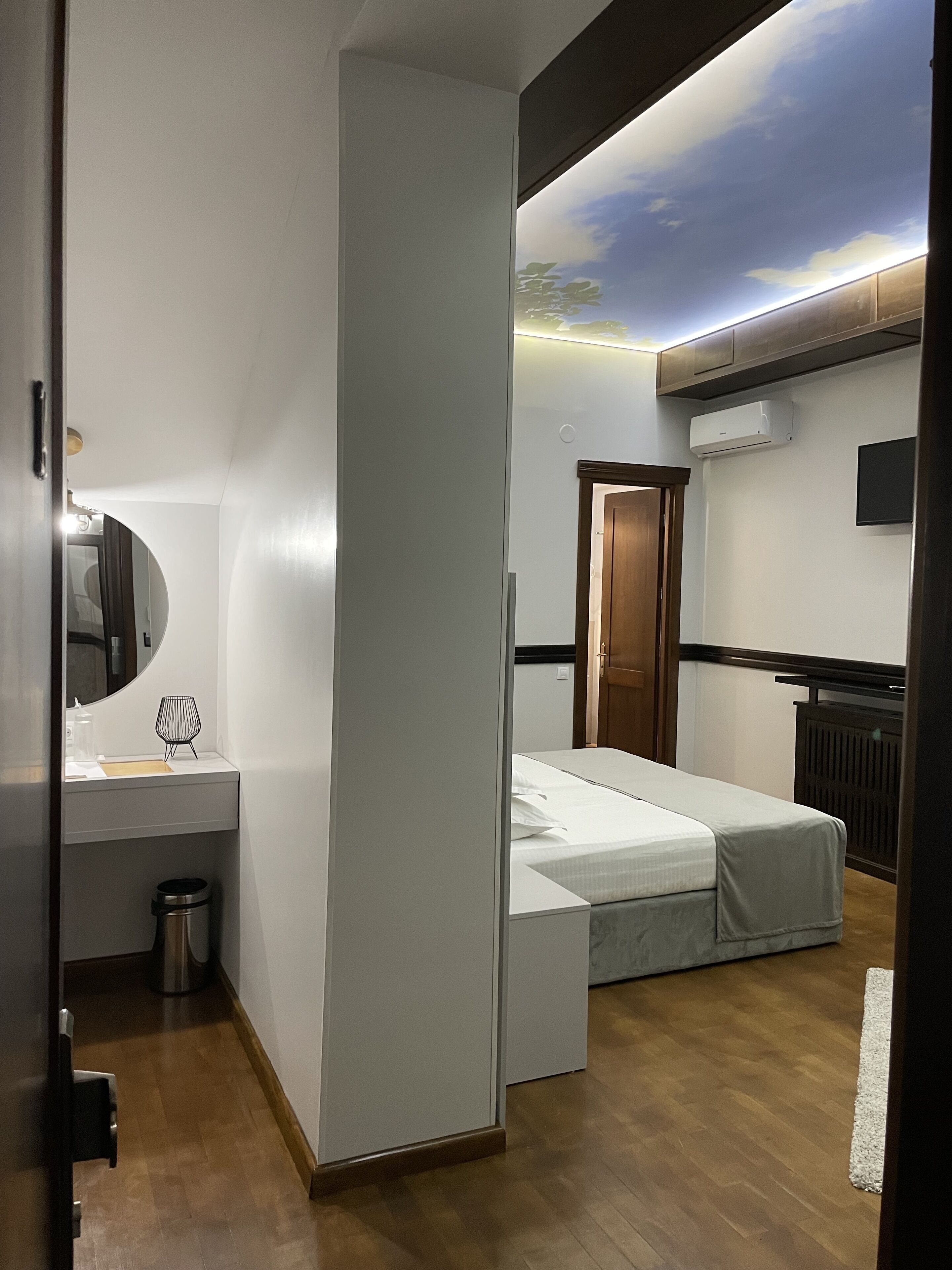 Habitación de hotel moderna con cama, mesita de noche, espejo y un mural en el techo.