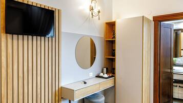 Un baño moderno con tocador de madera, espejo redondo, televisor montado y un estante pequeño con artículos de aseo.