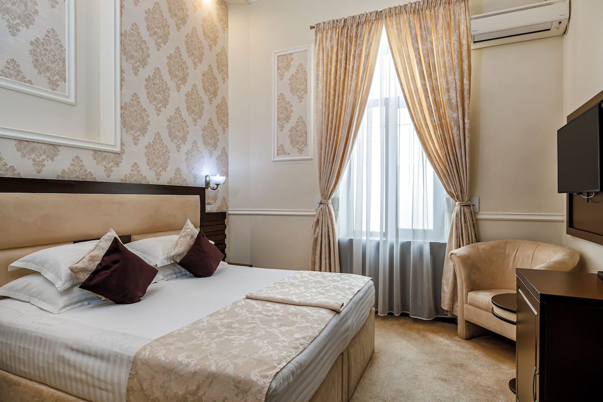 Una habitación de hotel con una cama grande, una silla, un escritorio y un equipo de aire acondicionado.