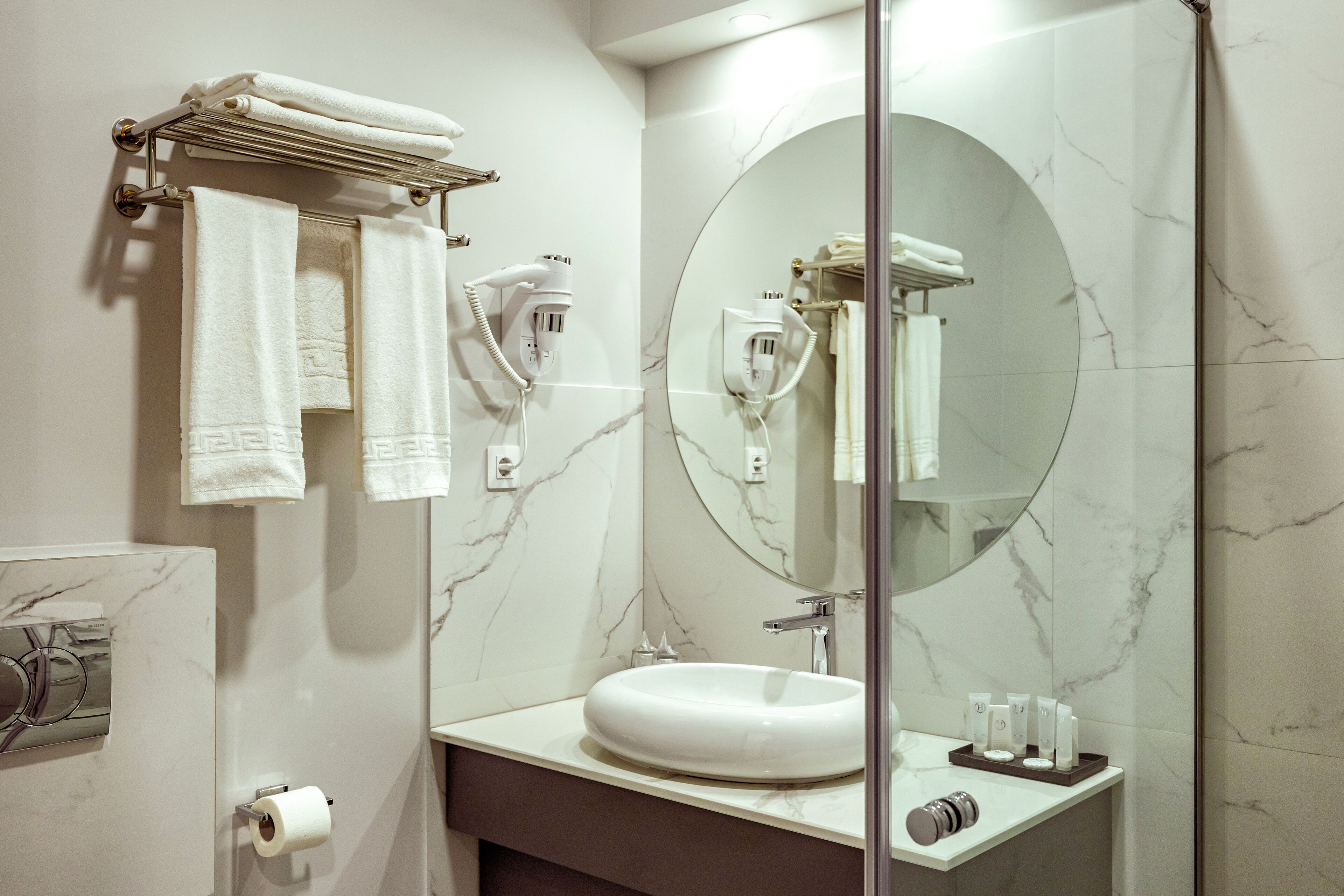 A bathroom with a marble sink, a large mirror, and a towel rack with folded towels.