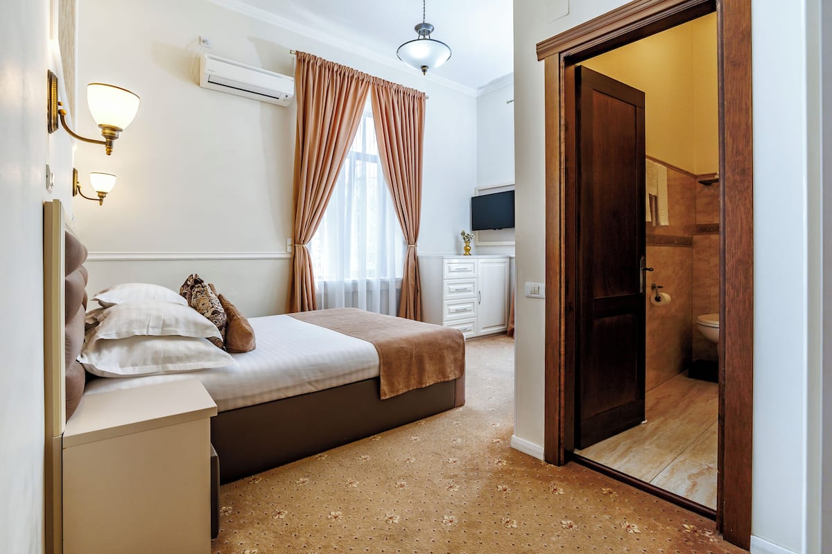 Un dormitorio con una cama, lámparas de noche, un televisor y un baño visible a través de una puerta abierta.