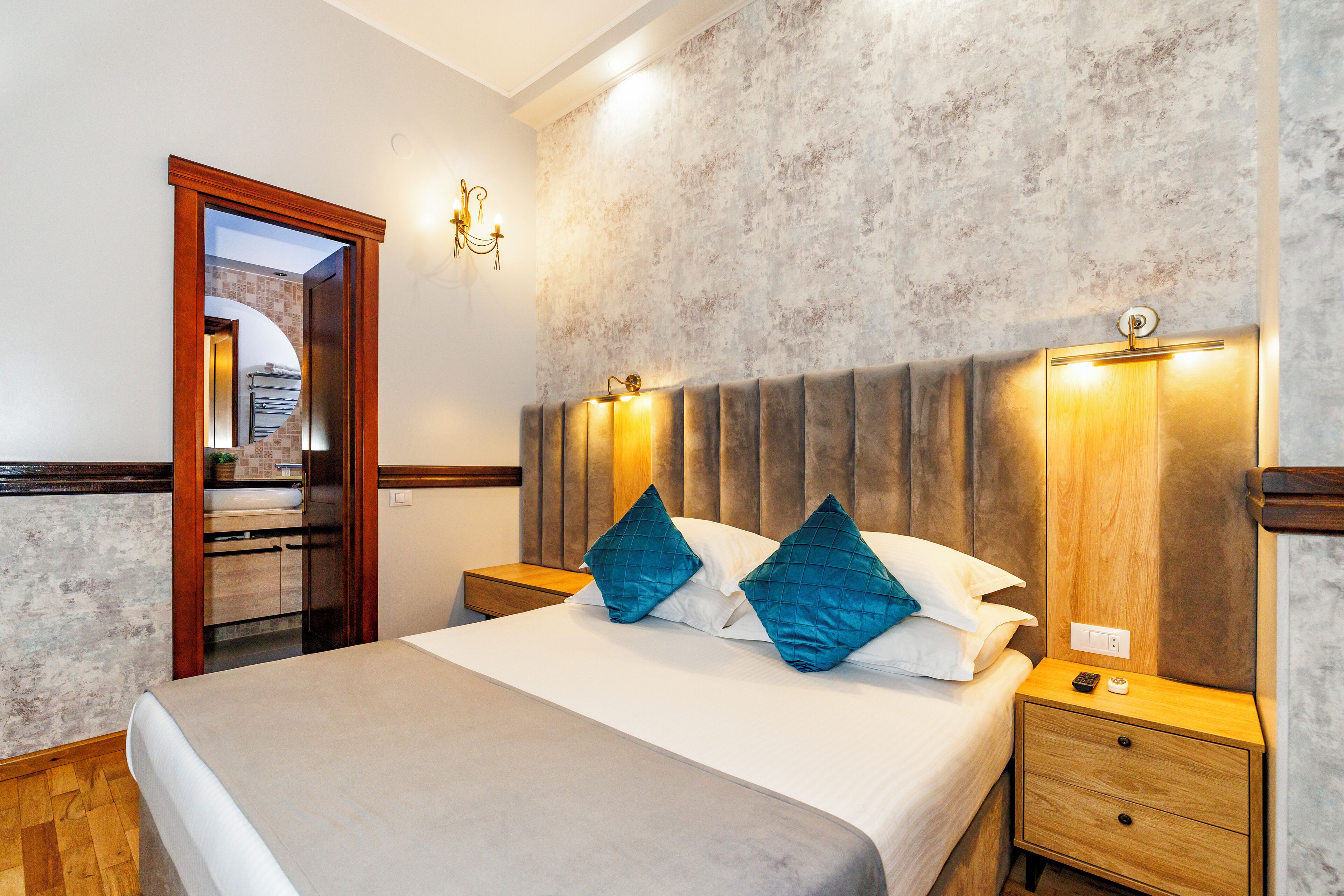 A neatly made bed with two pillows, a wooden nightstand with a lamp, and a wall-mounted light fixture.