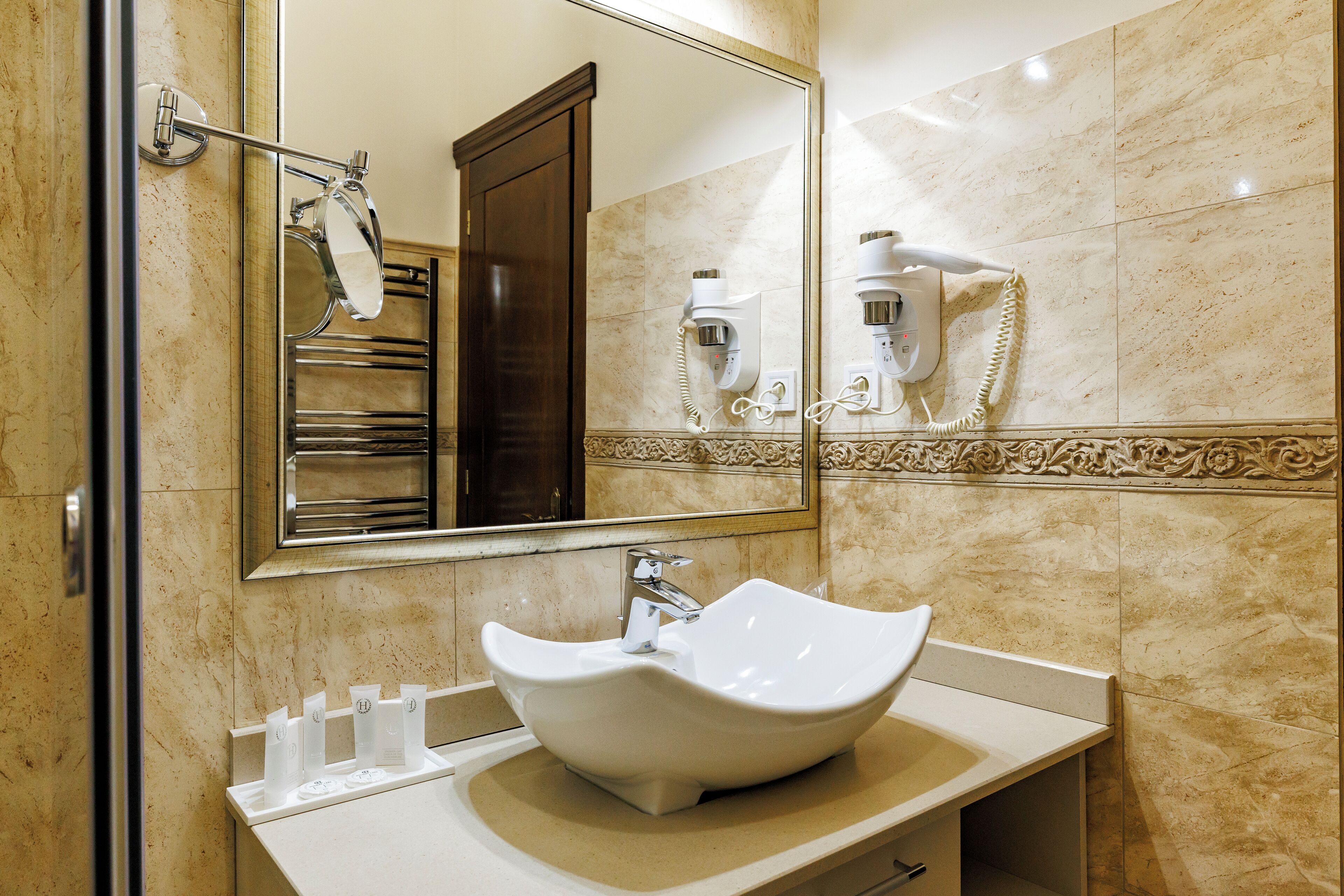 A bathroom with a large mirror, a white sink, and a hairdryer mounted on the wall.
