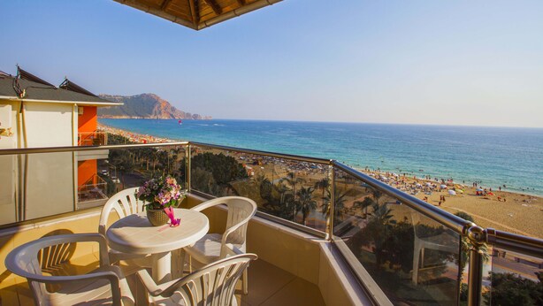 A balcony with a table and chairs, overlooking a beach with umbrellas and people. - Kleopatra Ada Beach Hotel (Alanya)