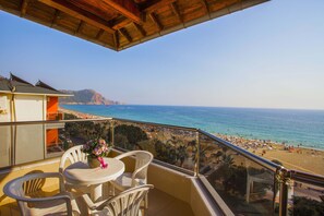 A balcony with a table and chairs, overlooking a beach with umbrellas and people. - Kleopatra Ada Beach Hotel (Alanya)