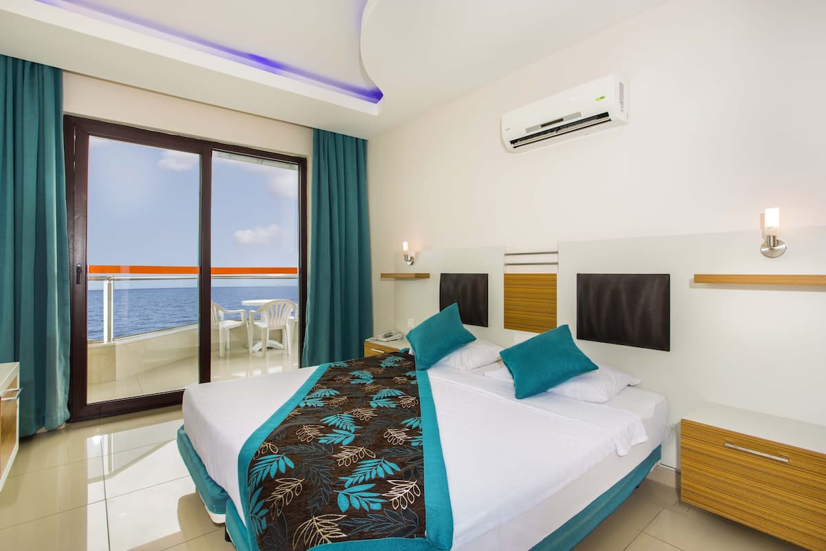 A hotel room with a bed, a nightstand, a desk, a chair, and a view of the ocean.