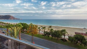 A coastal road with a beach and palm trees in the foreground, leading to a beach with umbrellas and people. - Kleopatra Ada Beach Hotel (Alanya)