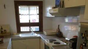 Eine Küche mit weißen Schränken, einem Fenster mit Aussicht, einer Spüle, einem Herd und einem Kühlschrank mit Magneten.