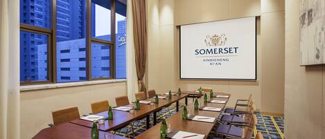 Een congrescentrum met een lange tafel, stoelen en een projectorscherm waarop het logo van Somerset Xindicheng XI'AN staat.