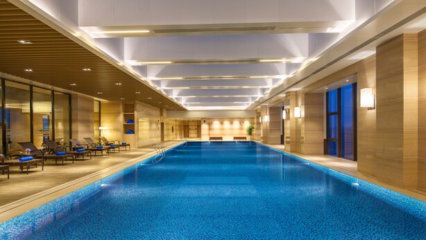 Una gran piscina interior con suelo de baldosas, rodeada de sillones de descanso y una pared de madera.