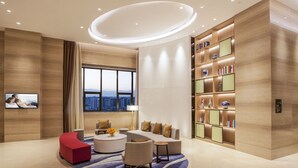Una sala de estar moderna con un sofá, un sillón rojo de acento y una mesa de centro redonda. Se observa una estantería con objetos decorativos y un televisor montado en la pared.
