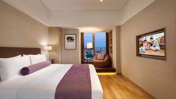 Habitación de hotel con una cama grande, televisión, una silla y vistas a la ciudad.