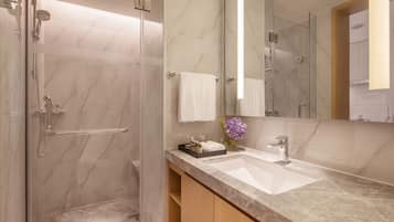 A modern bathroom with a glass-enclosed shower, a marble-tiled wall, a sink with a vanity, and a large mirror.