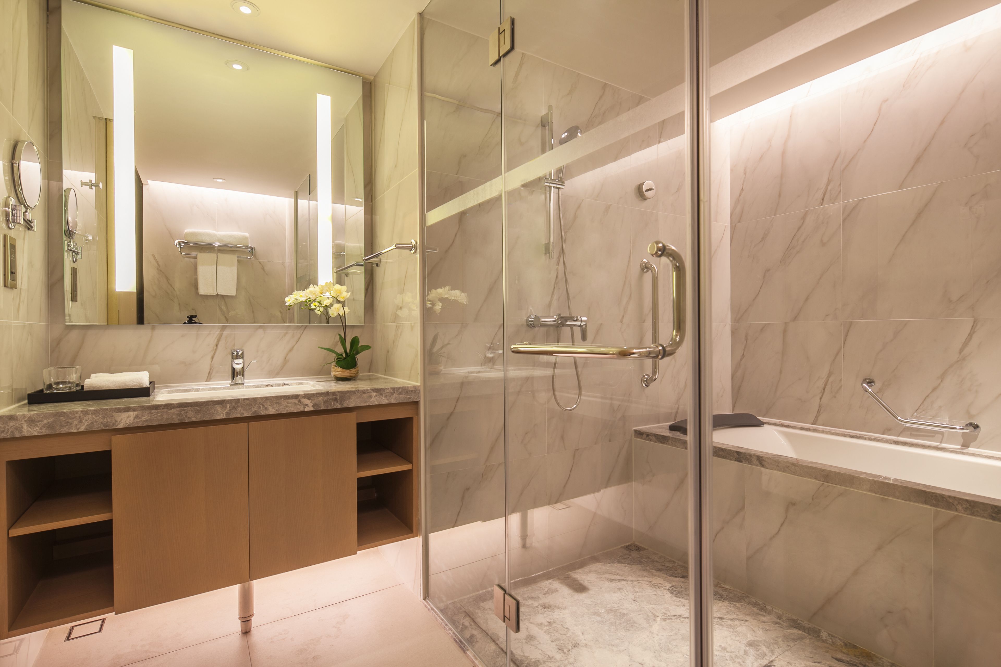 Une salle de bain moderne avec une douche à parois de verre, un mur recouvert de carreaux de marbre, un grand miroir et un meuble-lavabo en bois.