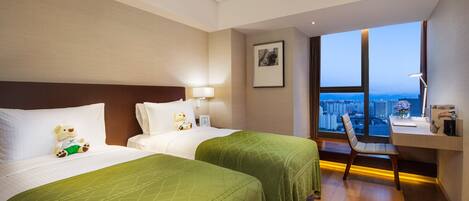 A hotel room with two beds, a desk, and a view of the city.