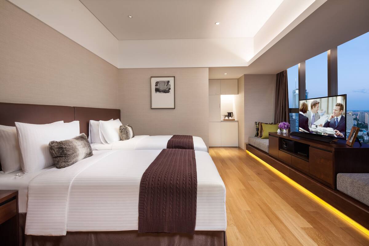 Een moderne hotelkamer met een groot bed, een bureau met een computer en een groot raam met uitzicht op de stad.