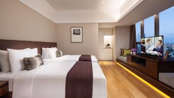 A modern hotel room with a large bed, a desk with a computer, and a large window with a city view.