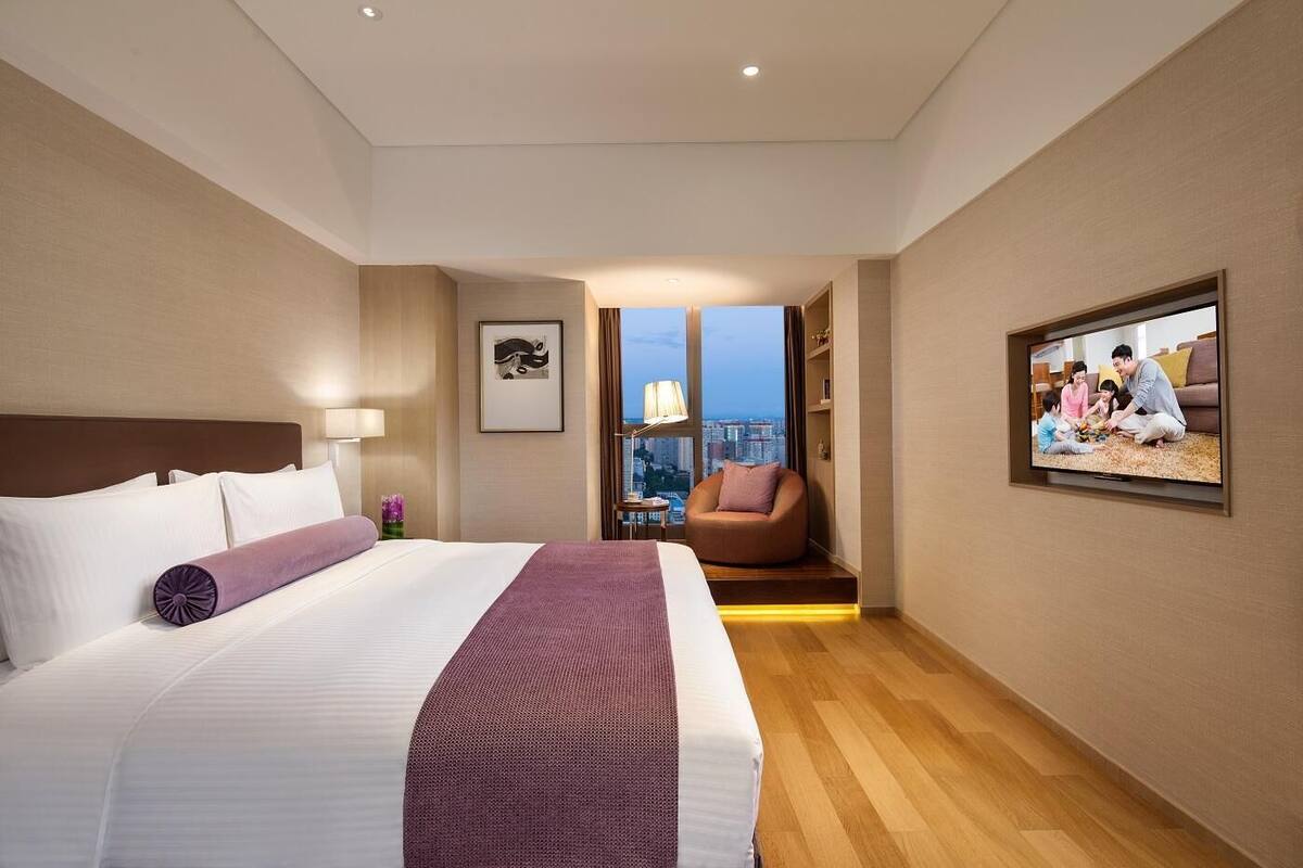 Een hotelkamer met een groot bed, een televisie, een stoel en uitzicht op de stad.