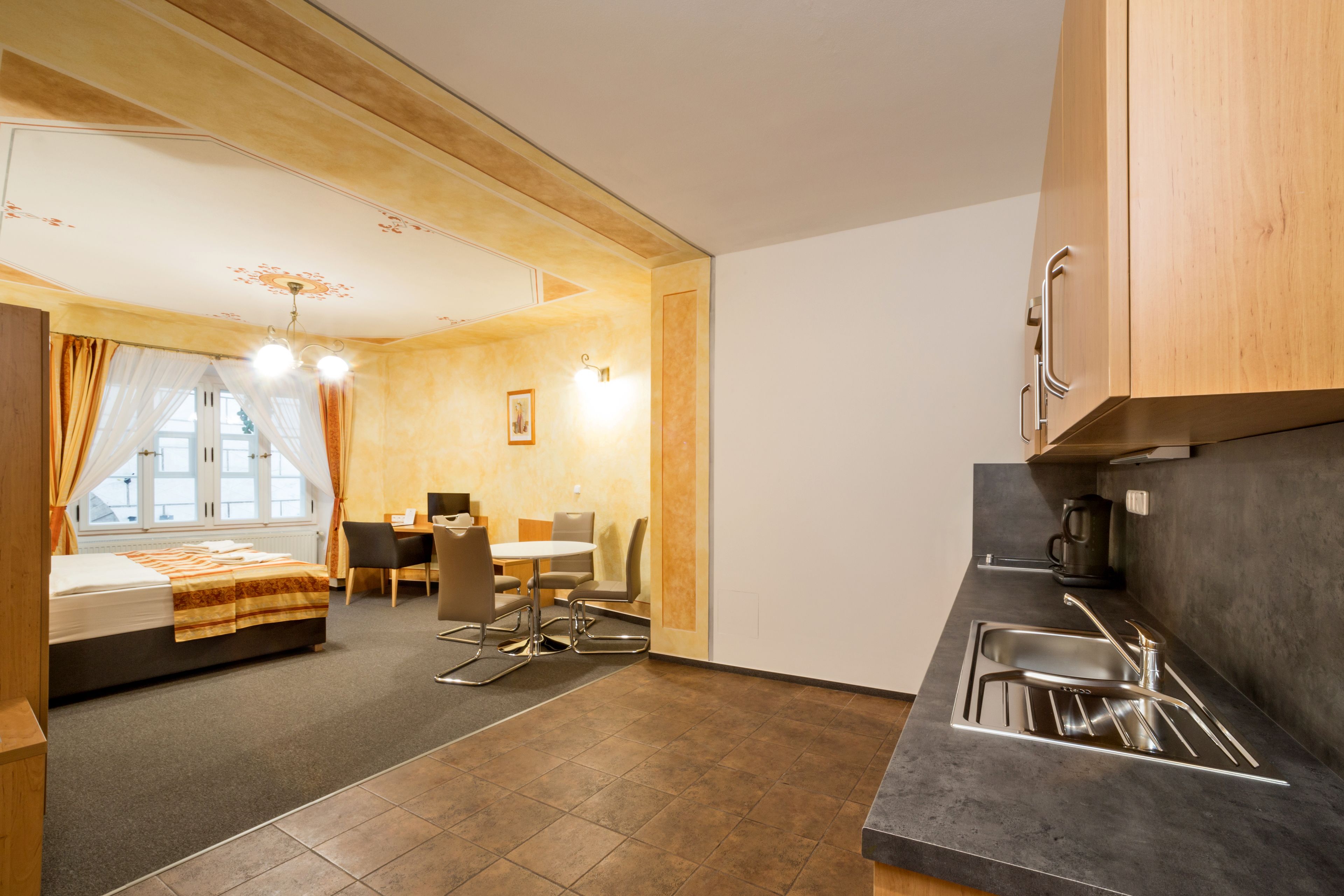 Habitación de hotel compacta con cama, una mesa de comedor, sillas, kitchenette y una ventana con cortinas.