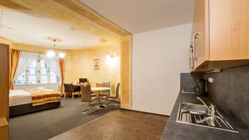 Habitación de hotel compacta con cama, una mesa de comedor, sillas, kitchenette y una ventana con cortinas.