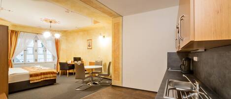 Habitación de hotel compacta con cama, una mesa de comedor, sillas, kitchenette y una ventana con cortinas.