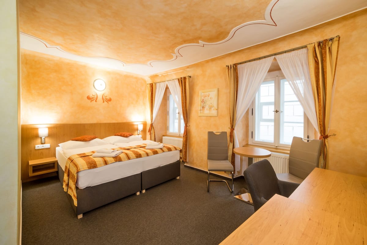 Una habitación de hotel con cama, una silla, una mesa y una ventana con cortinas.