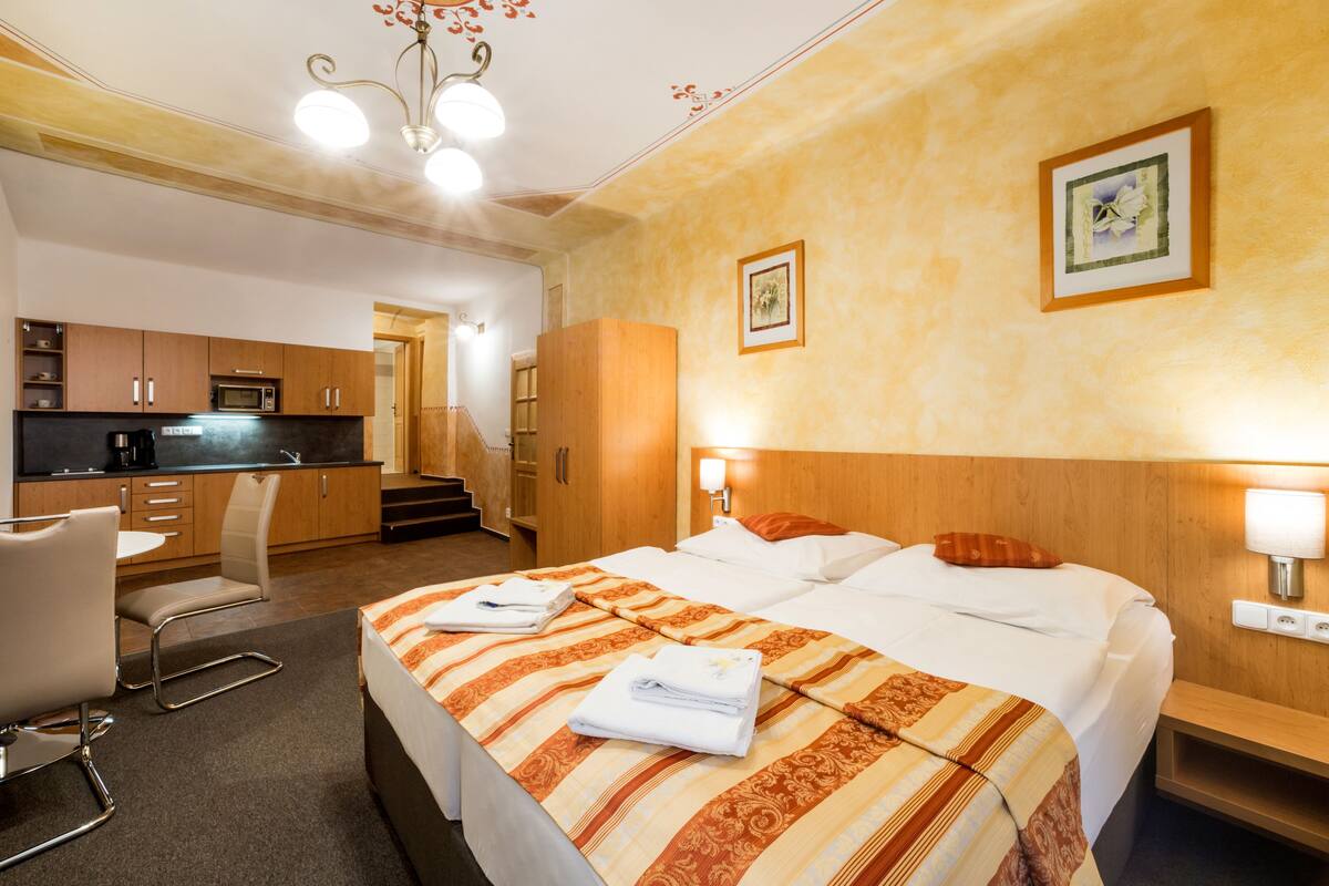 Una habitación de hotel con cama, mesita de noche y un espacio con kitchenette.