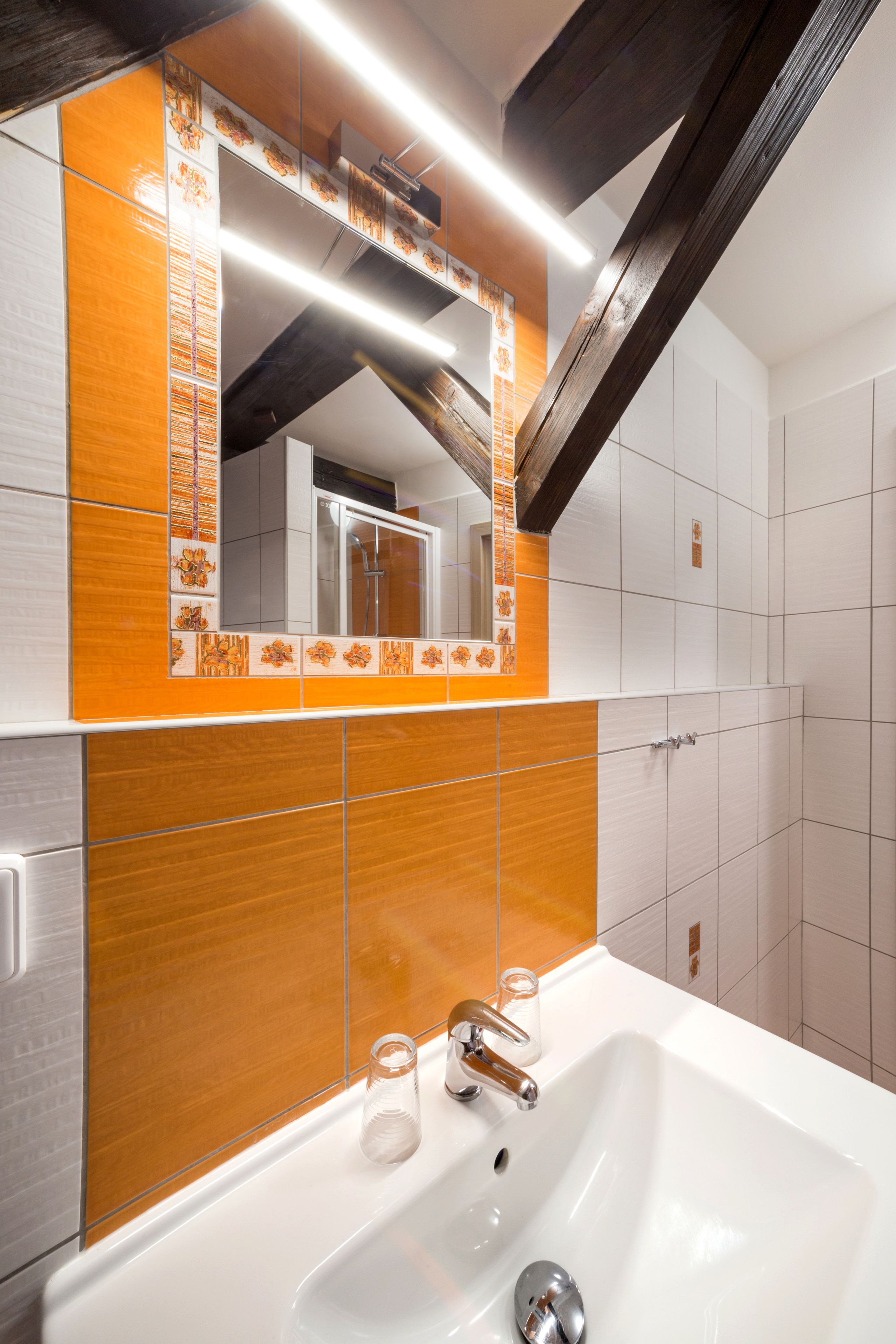 A modern bathroom with a white sink, orange-tiled backsplash, and a large mirror.