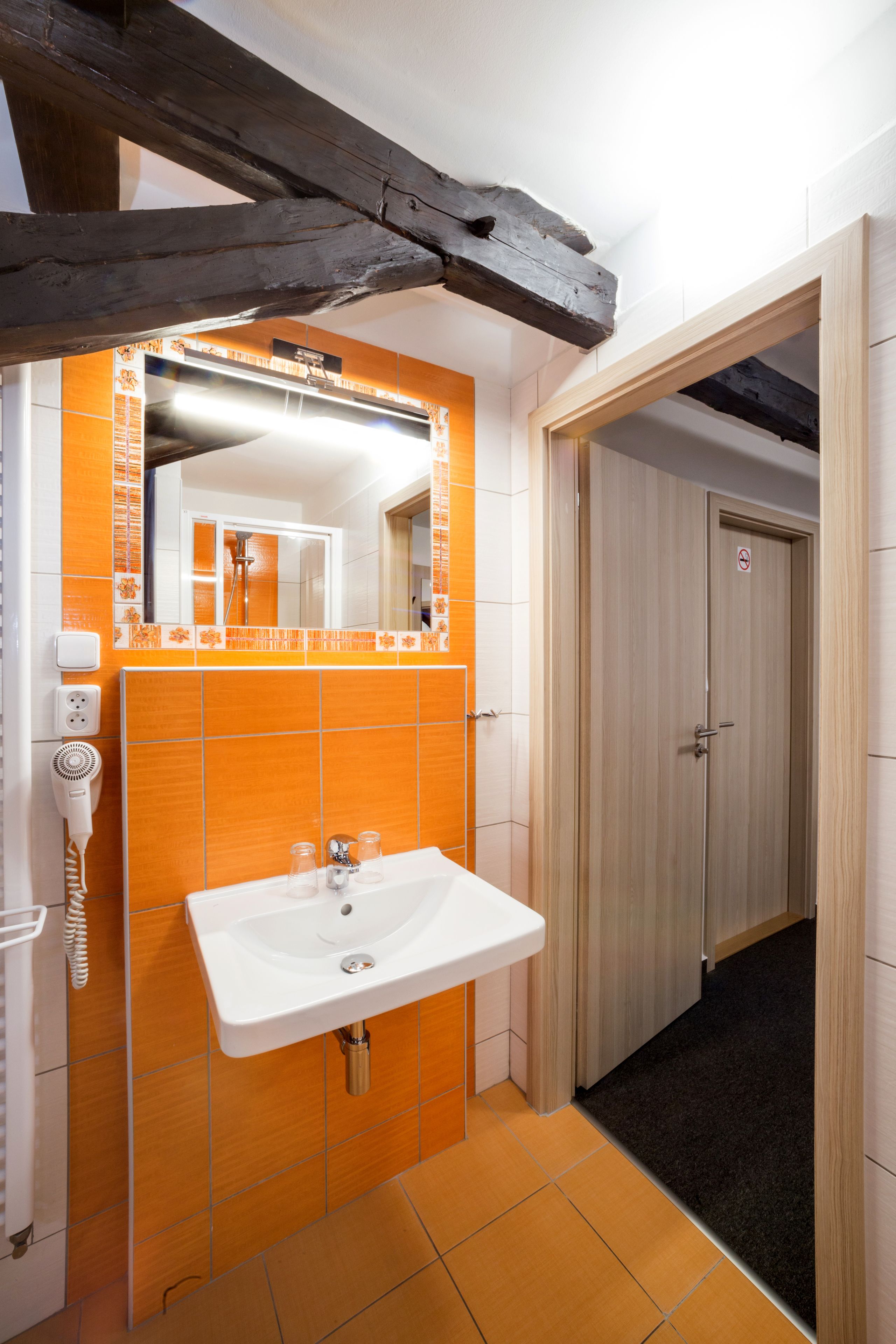 Een badkamer met een oranje betegelde muur, een witte wastafel en een spiegel erboven.